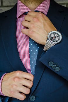 Stylish man adjusting tie, showcasing formal suit and luxury wristwatch.