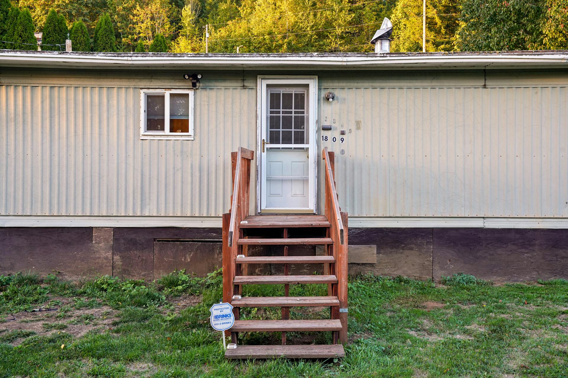 Exterior view of a mobile home with wooden steps on a sunny day.