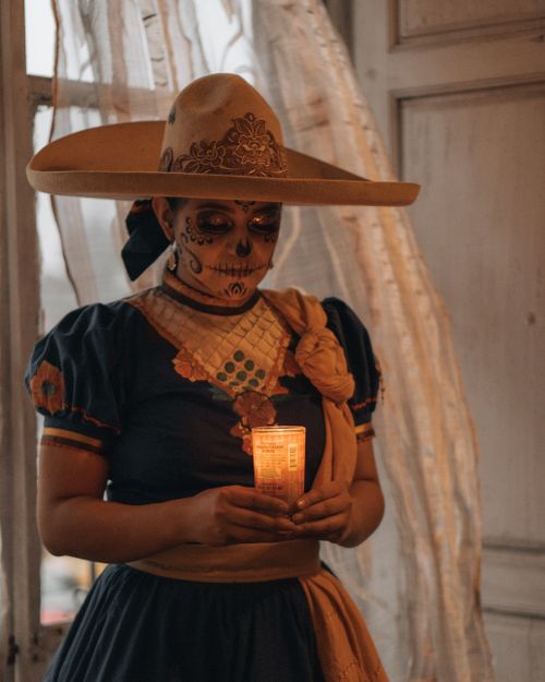 Free Person in Day of the Dead costume with candle indoors, evoking traditional Mexican culture. Stock Photo