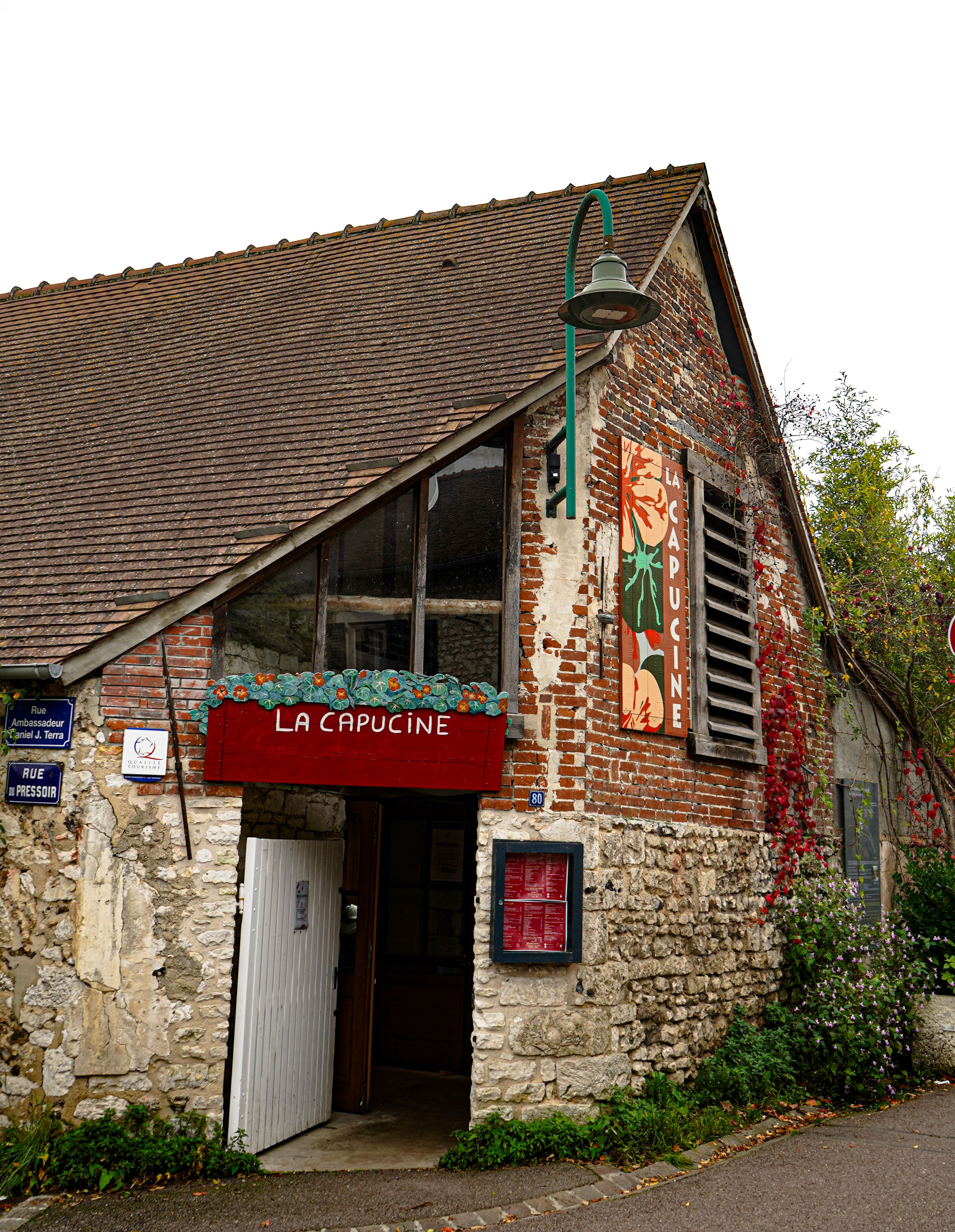 Rustic exterior of La Capucine bistro in Giverny, France with brick and stone facade.