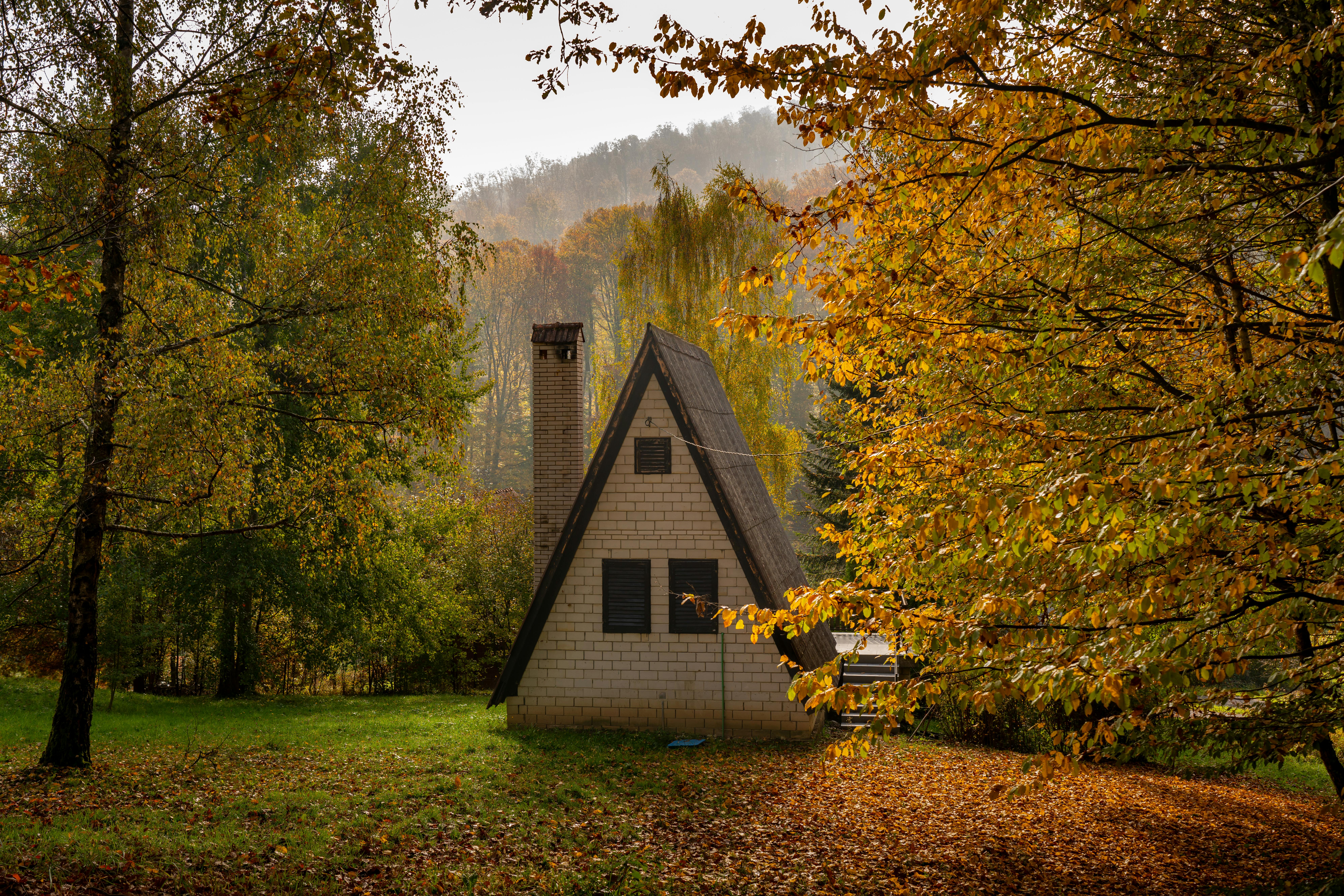 A picturesque A-frame cabin surrounded by vibrant autumn foliage in Podgarić, Croatia.