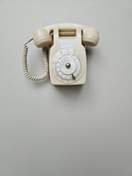 Vintage cream rotary dial telephone mounted on a plain wall, classic retro style.