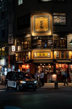 A vibrant night scene of a traditional Japanese restaurant with a taxi in the foreground.