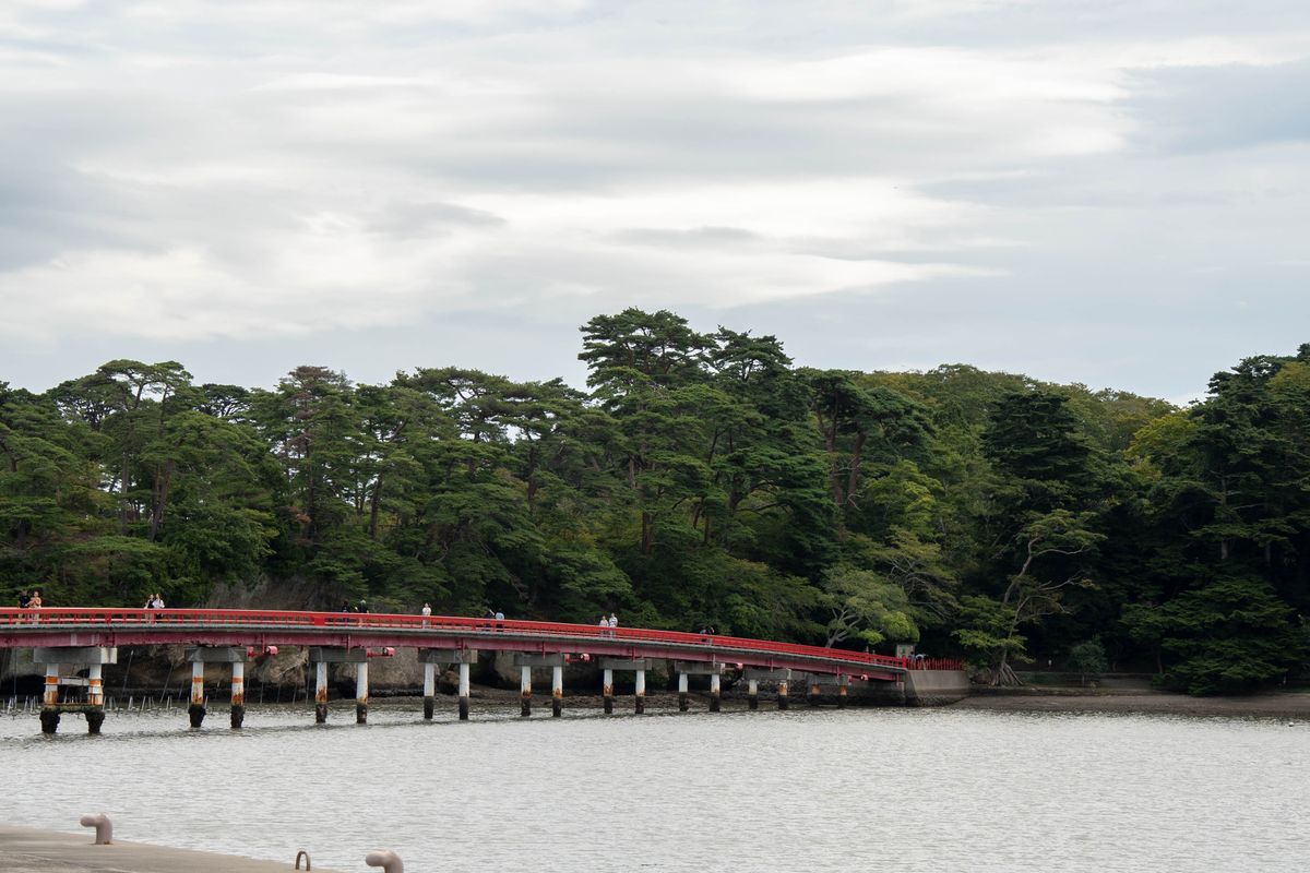 A long red footbridge leading across the water to a pine-covered island in Matsushima