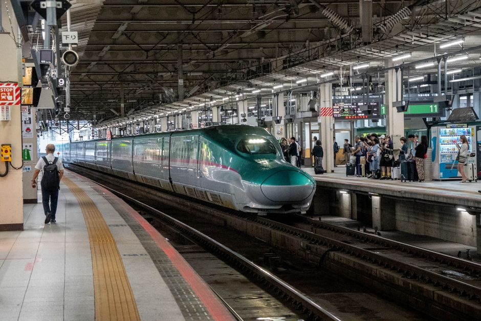 A high-speed Shinkansen train arrives at a bustling Japanese train station.