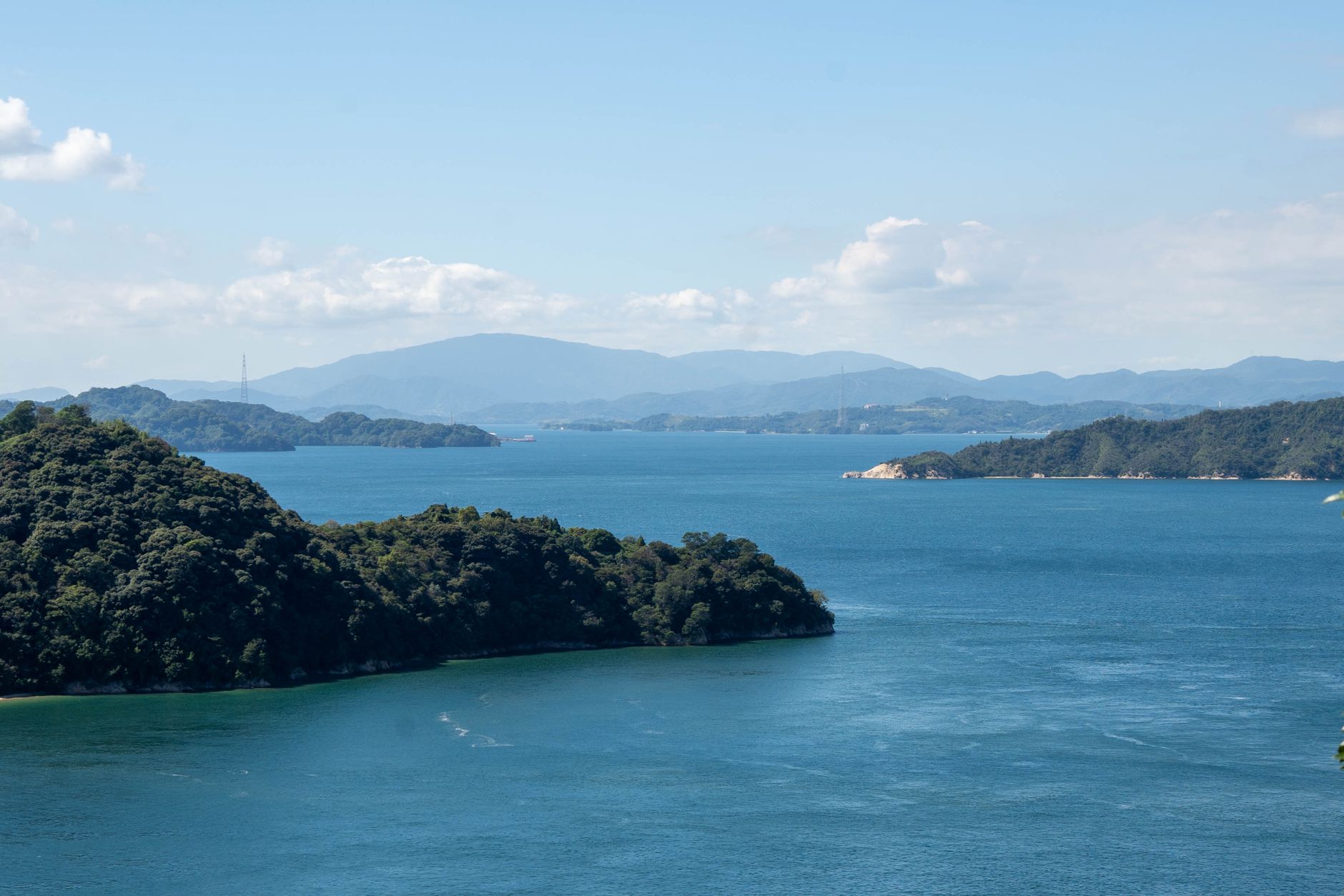 A tranquil scene featuring blue water, green islands, and a distant mountain under a clear sky.
