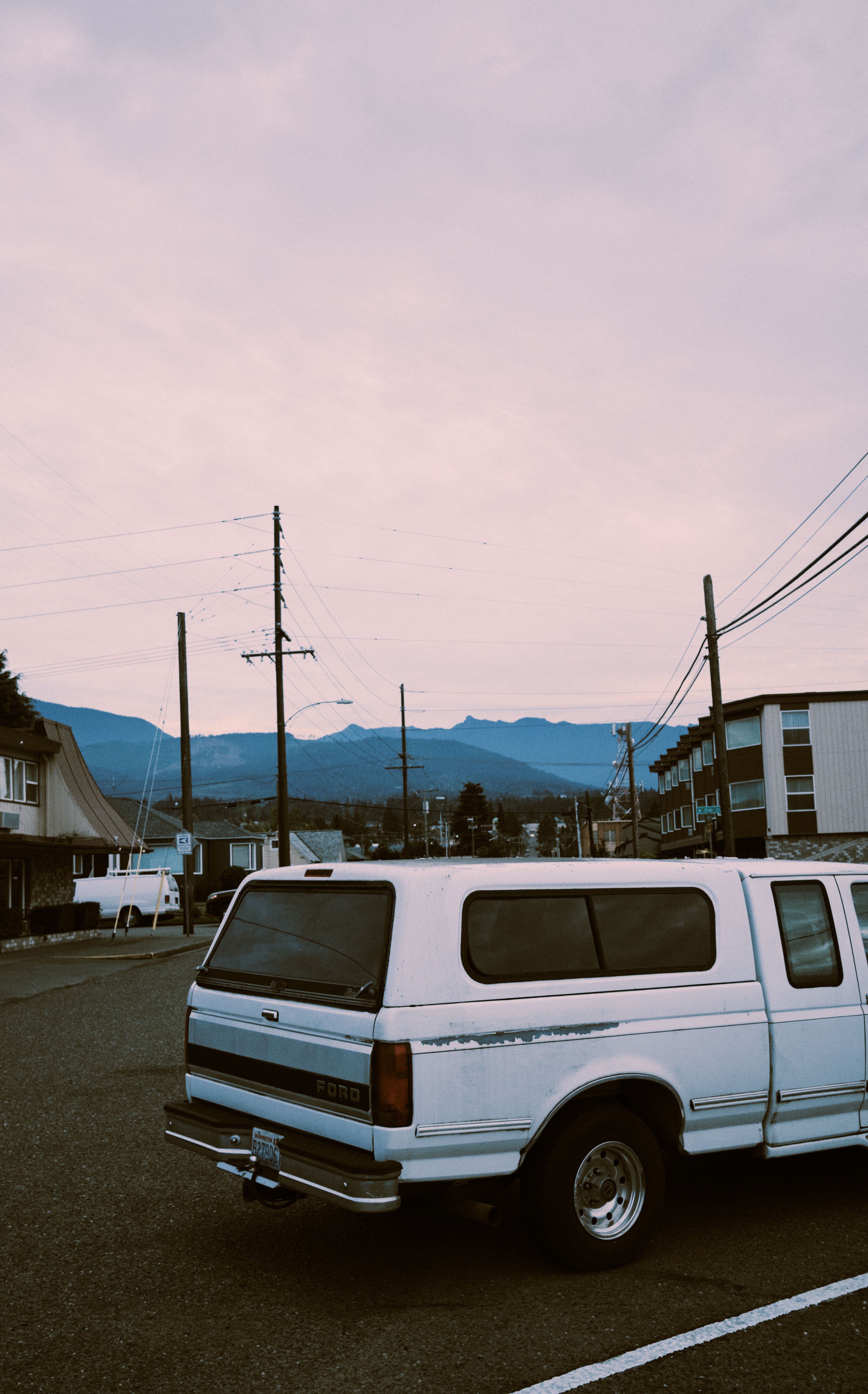 A vintage pickup truck parked on a quiet street with mountains in the background, during day time.