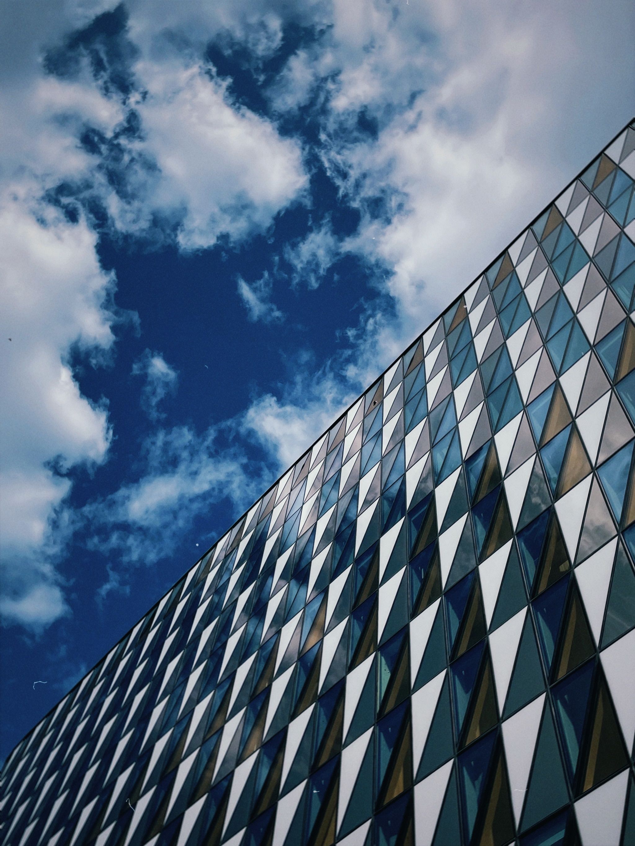 Gratis Samtidsarkitektur med geometriske mønstre som reflekterer en lys blå himmel med skyer. Arkivbilde