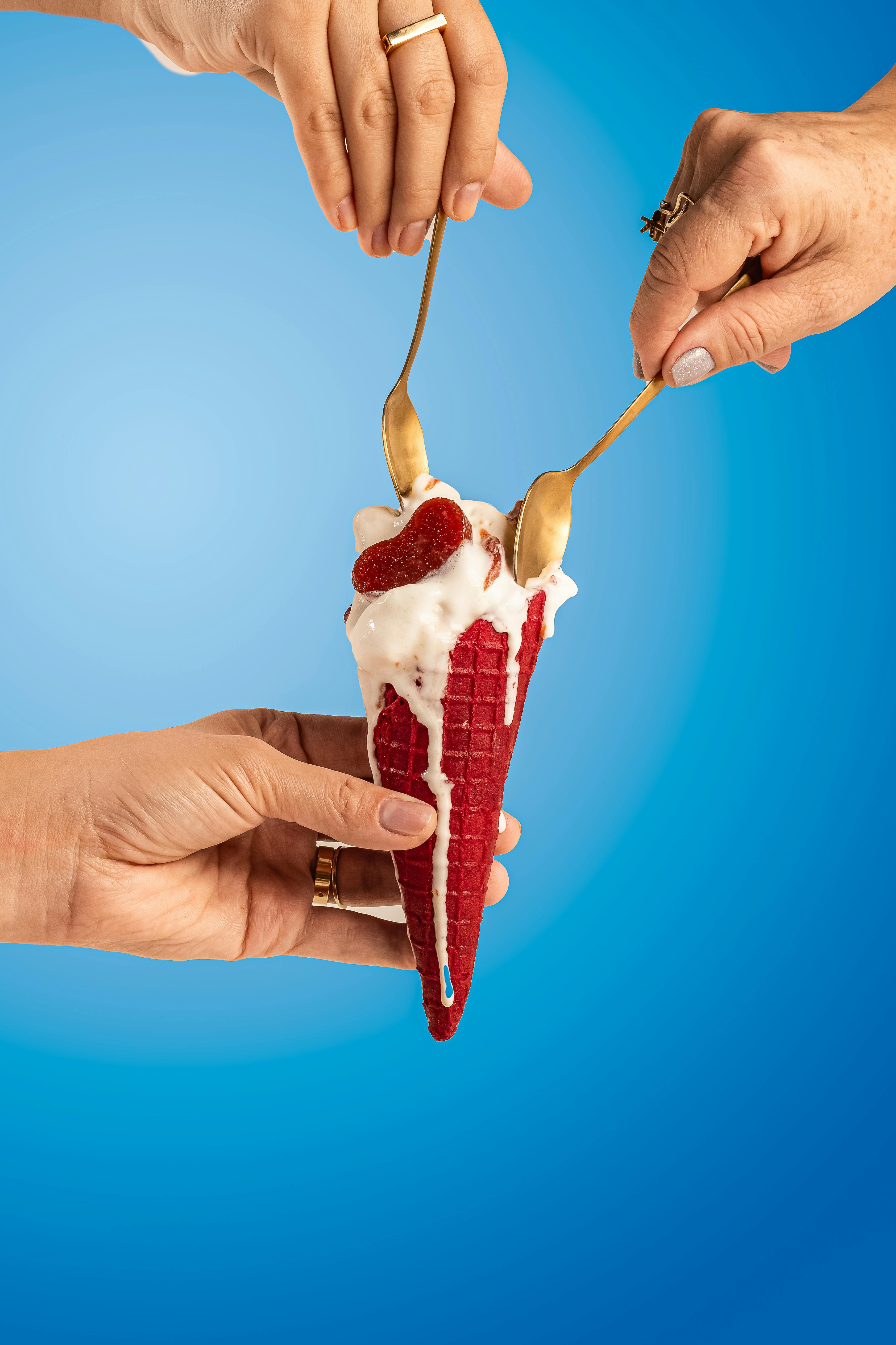 Strawberry ice cream in a red cone shared with golden spoons.