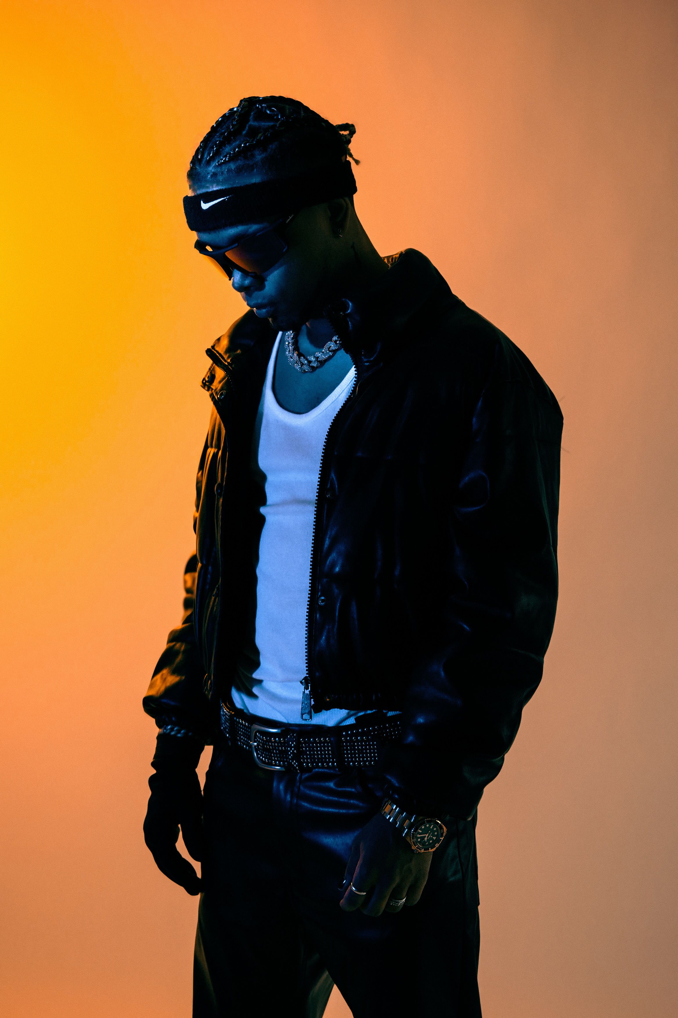 Fashionable musician in leather, sunglasses, and jewelry under dramatic lighting.
