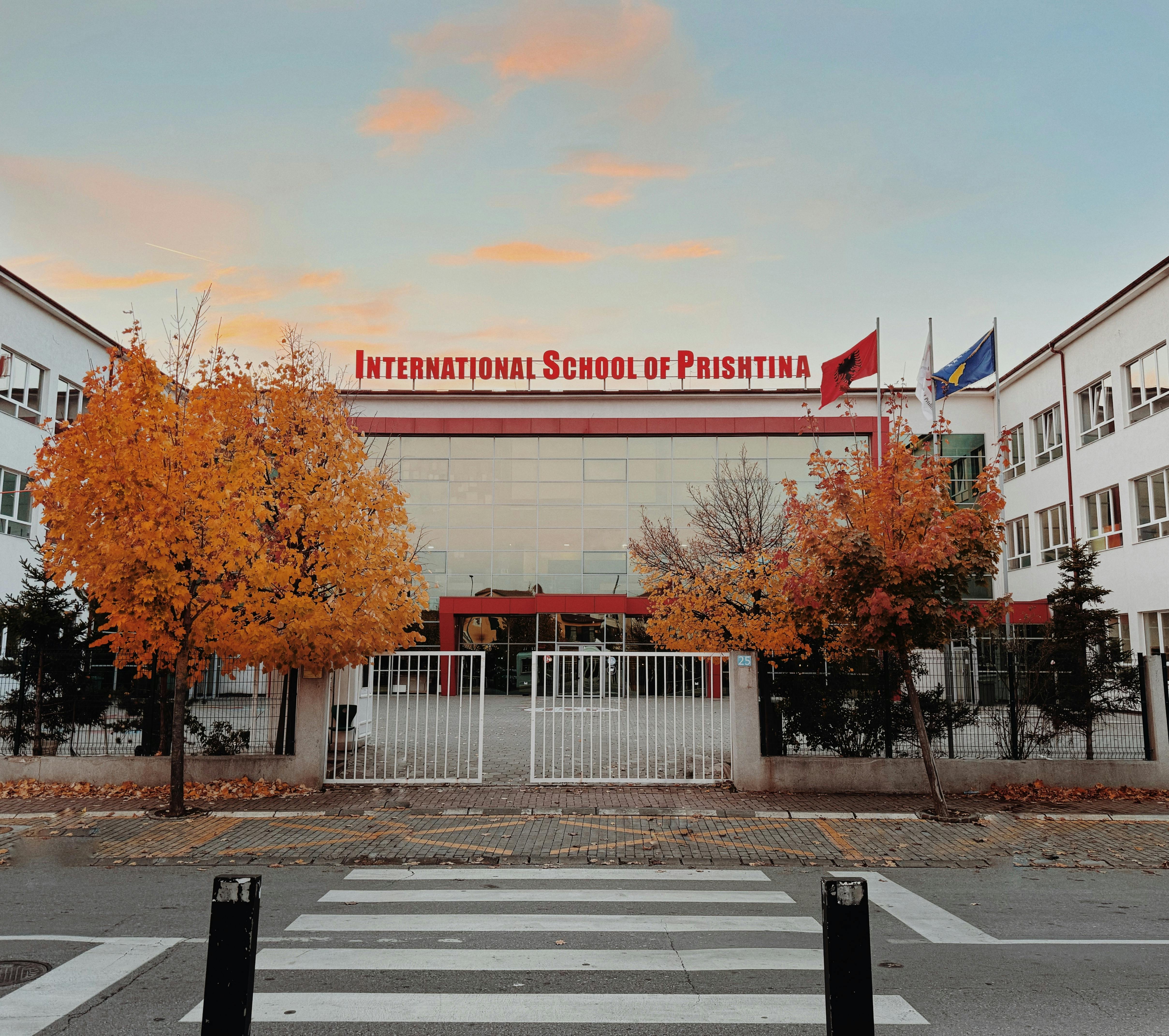 Front view of International School of Prishtina with autumn trees and flags.