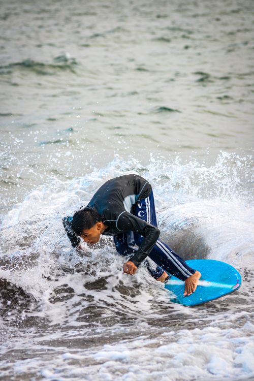 Free Surfer skillfully maneuvers through ocean waves with blue surfboard creating a splash. Stock Photo