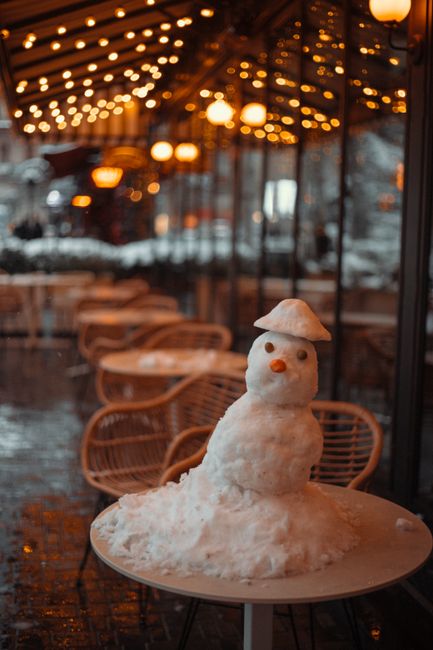 Charming snowman on table in a Baku café with warm, festive lighting.