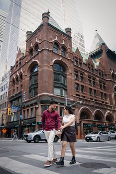 A couple walking hand in hand by historic buildings in downtown Toronto.