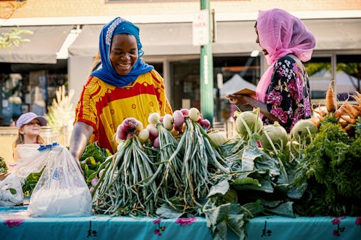Two women engage in friendly commerce at a colorful outdoor vegetable market.