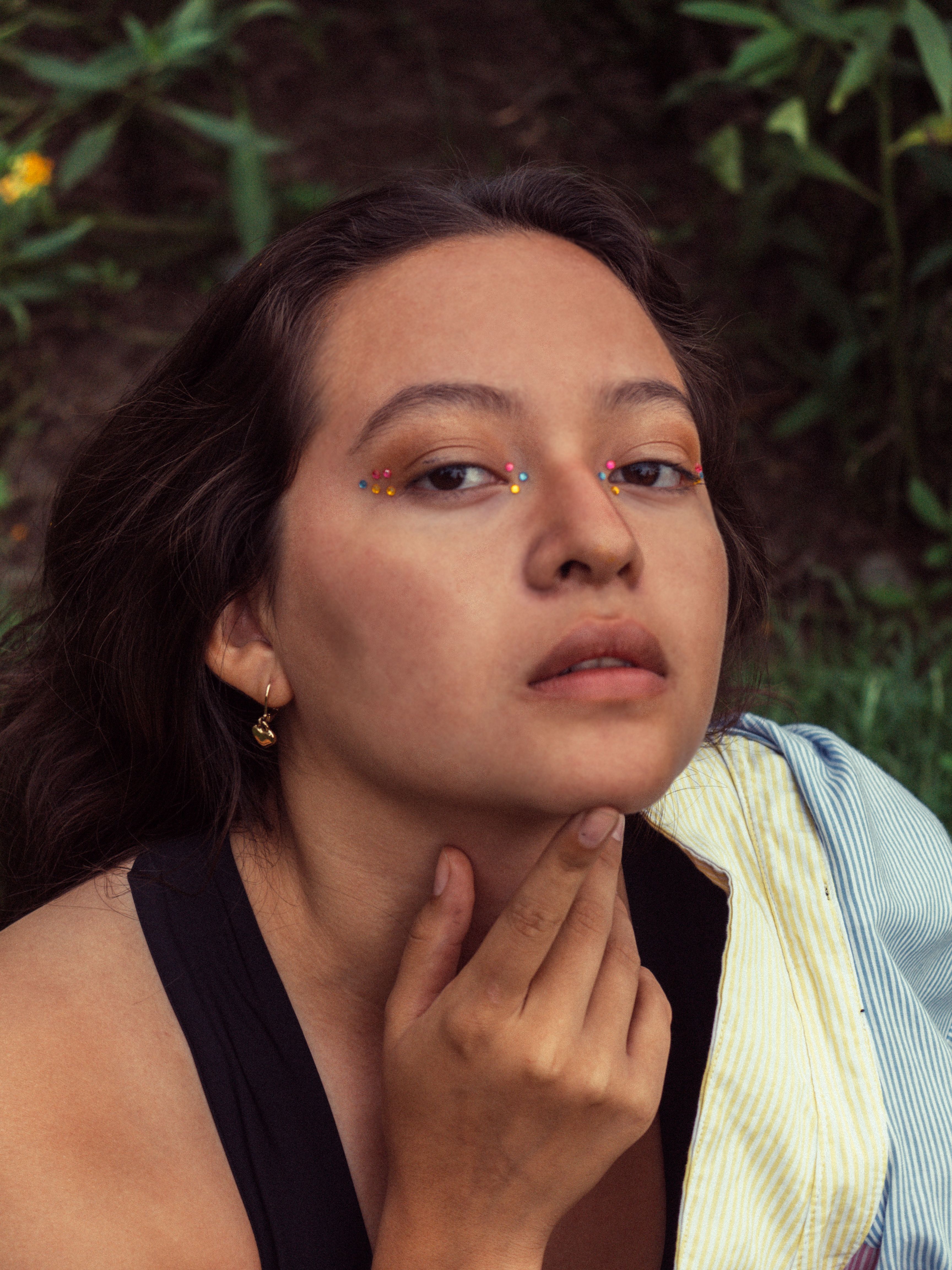 Intriguing outdoor portrait of a woman with colorful makeup and pensive expression.