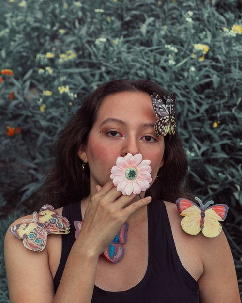 Free A woman holds a flower to her face surrounded by artistic butterflies. Stock Photo