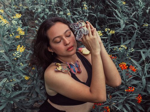 Free A serene woman surrounded by colorful butterflies in a vibrant garden setting. Stock Photo