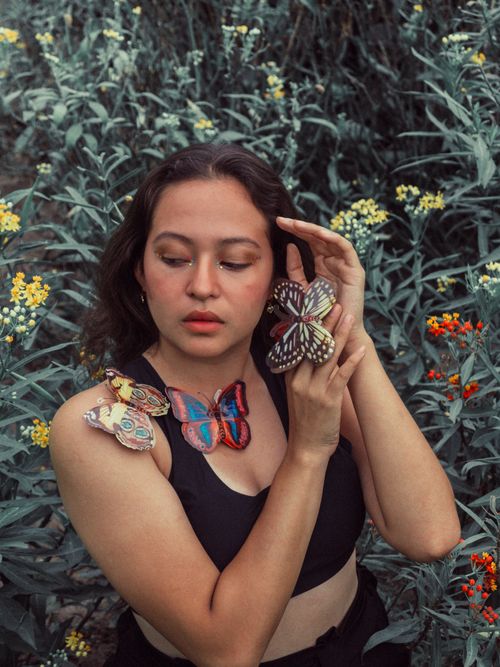 Free Young woman adorned with colorful butterflies in a lush floral environment. Stock Photo