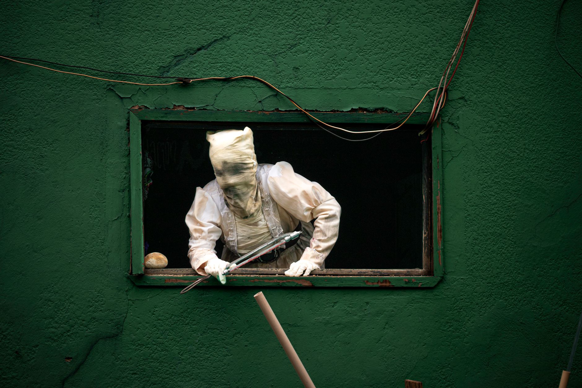 A mysterious figure peeking out of a window in an urban setting evokes themes of horror and intrigue.