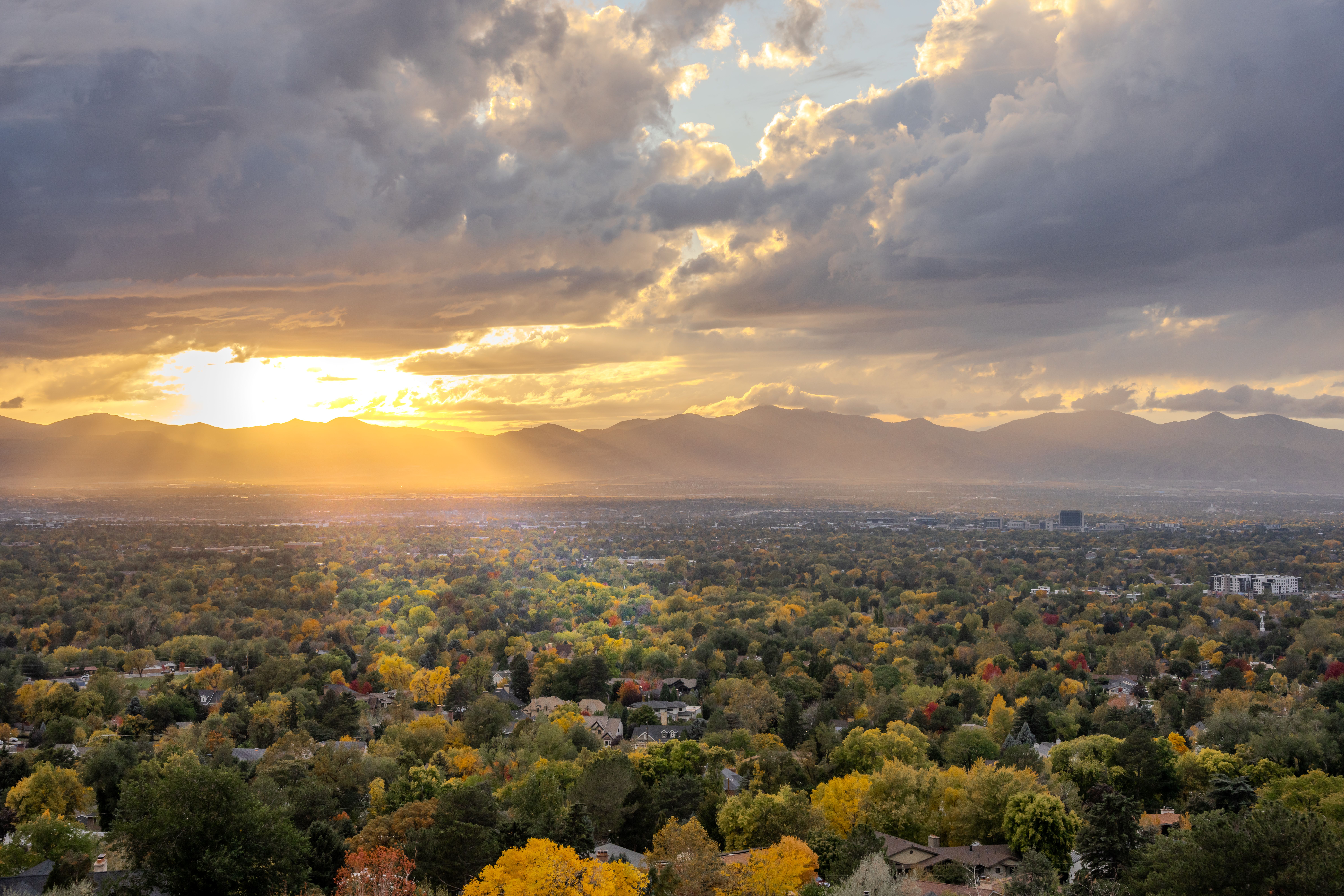 A stunning autumn sunset over a city with vibrant fall foliage and distant mountains.