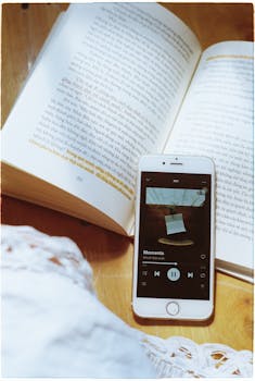 Close-up of an open book with a smartphone displaying a music app, creating a cozy reading ambiance.