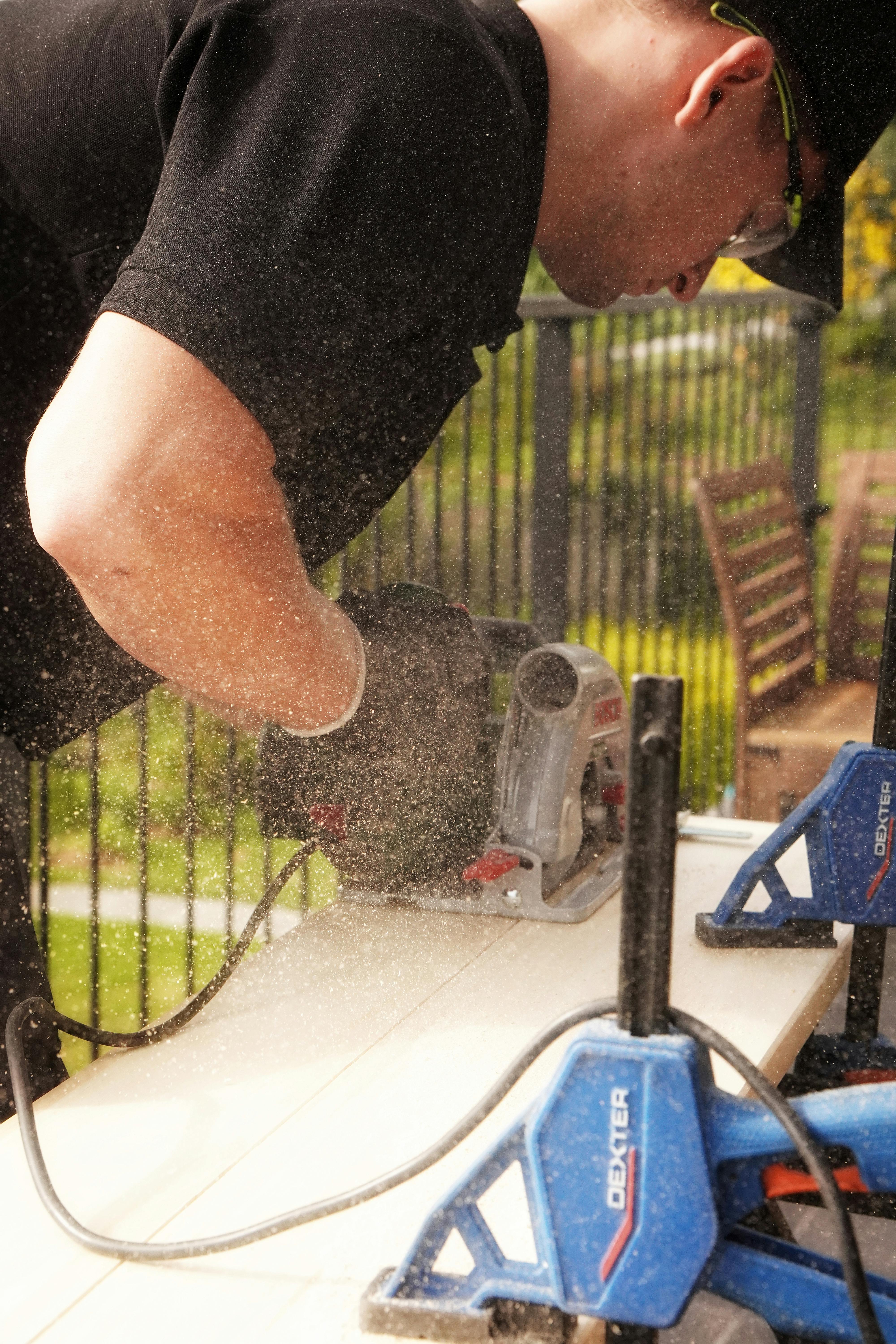 A carpenter skillfully cuts wood with power saw outdoors, creating sawdust.