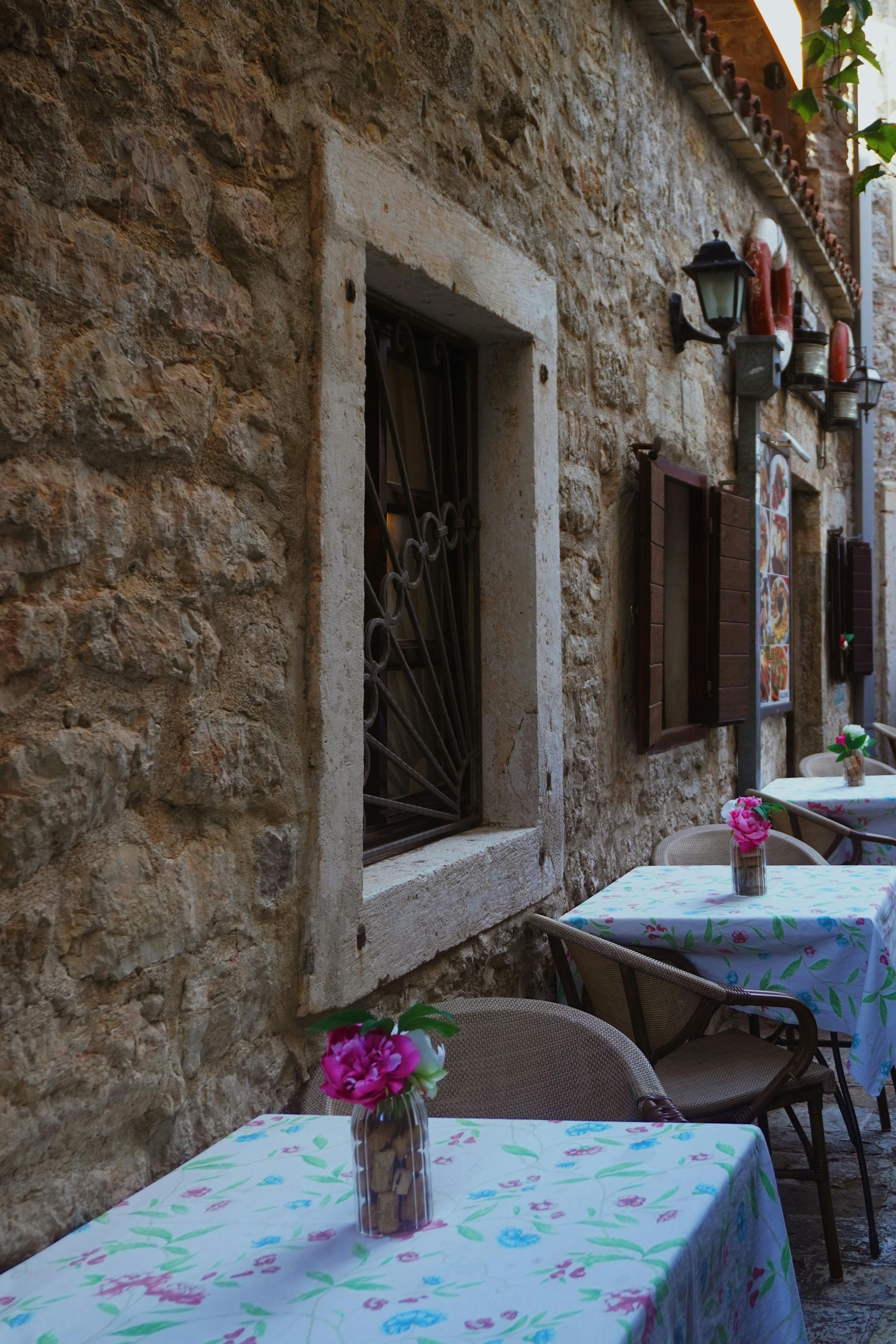 Cozy alleyway cafe with floral table decor in historic Budva, Montenegro.