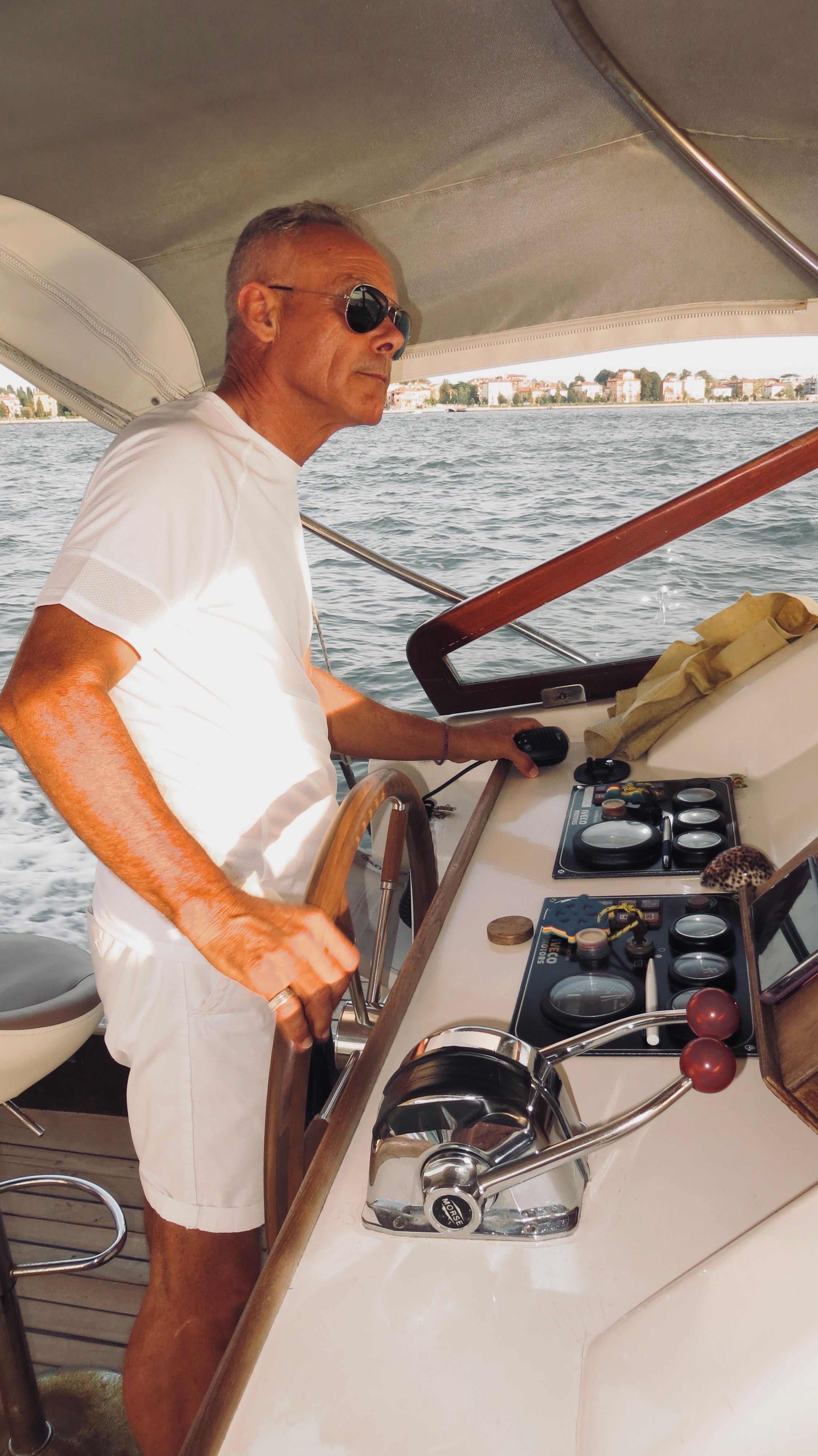 Senior male captain steering a yacht in Venice, Italy, under sunny skies.