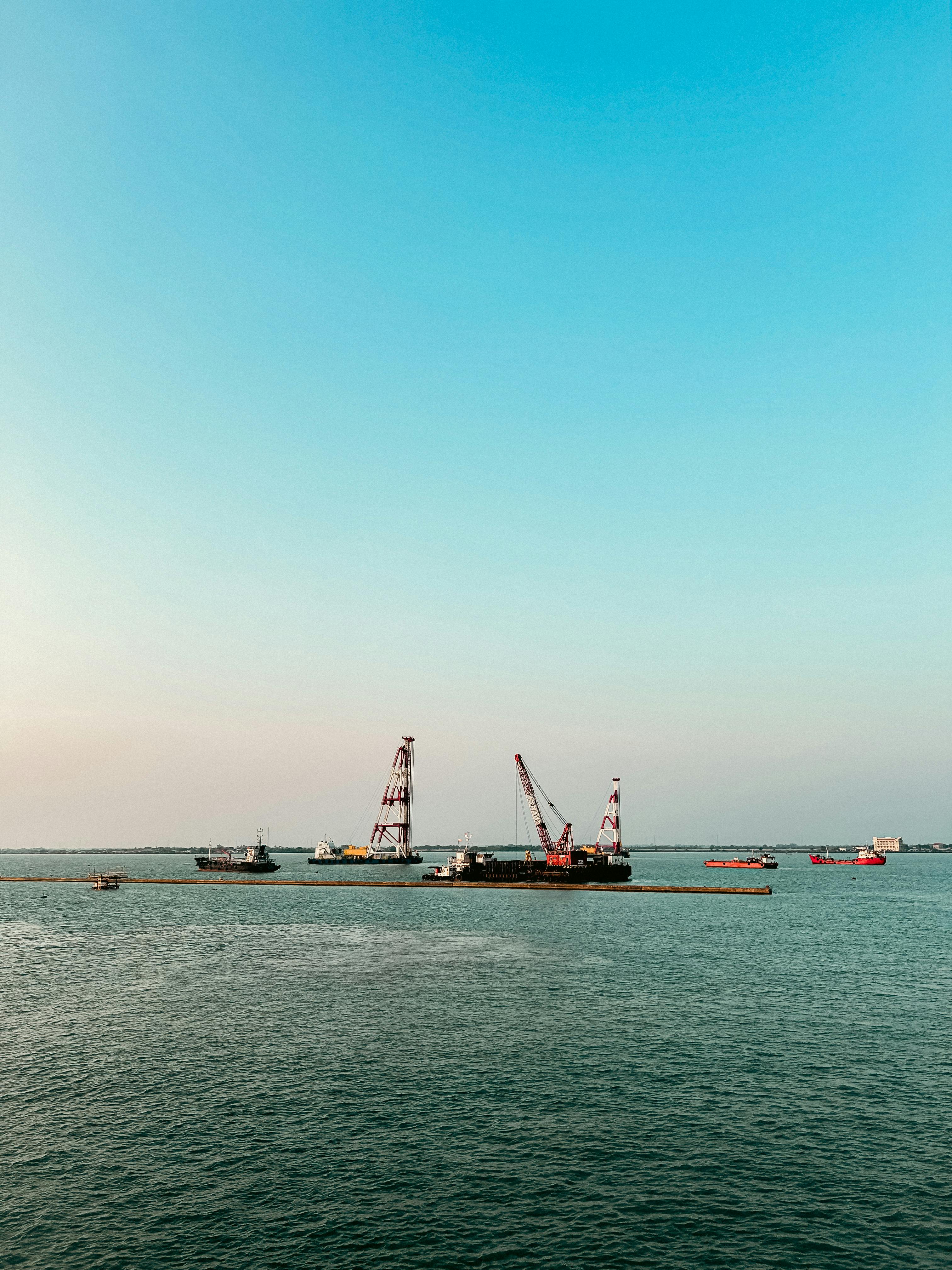 Aerial view of a busy harbor with anchored boats and construction cranes under a clear blue sky in Indonesia.