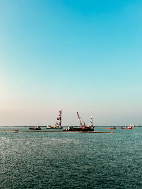 Aerial view of a busy harbor with anchored boats and construction cranes under a clear blue sky in Indonesia.