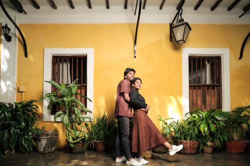 Free Happy couple embraces in front of a vibrant yellow wall surrounded by lush plants. Stock Photo
