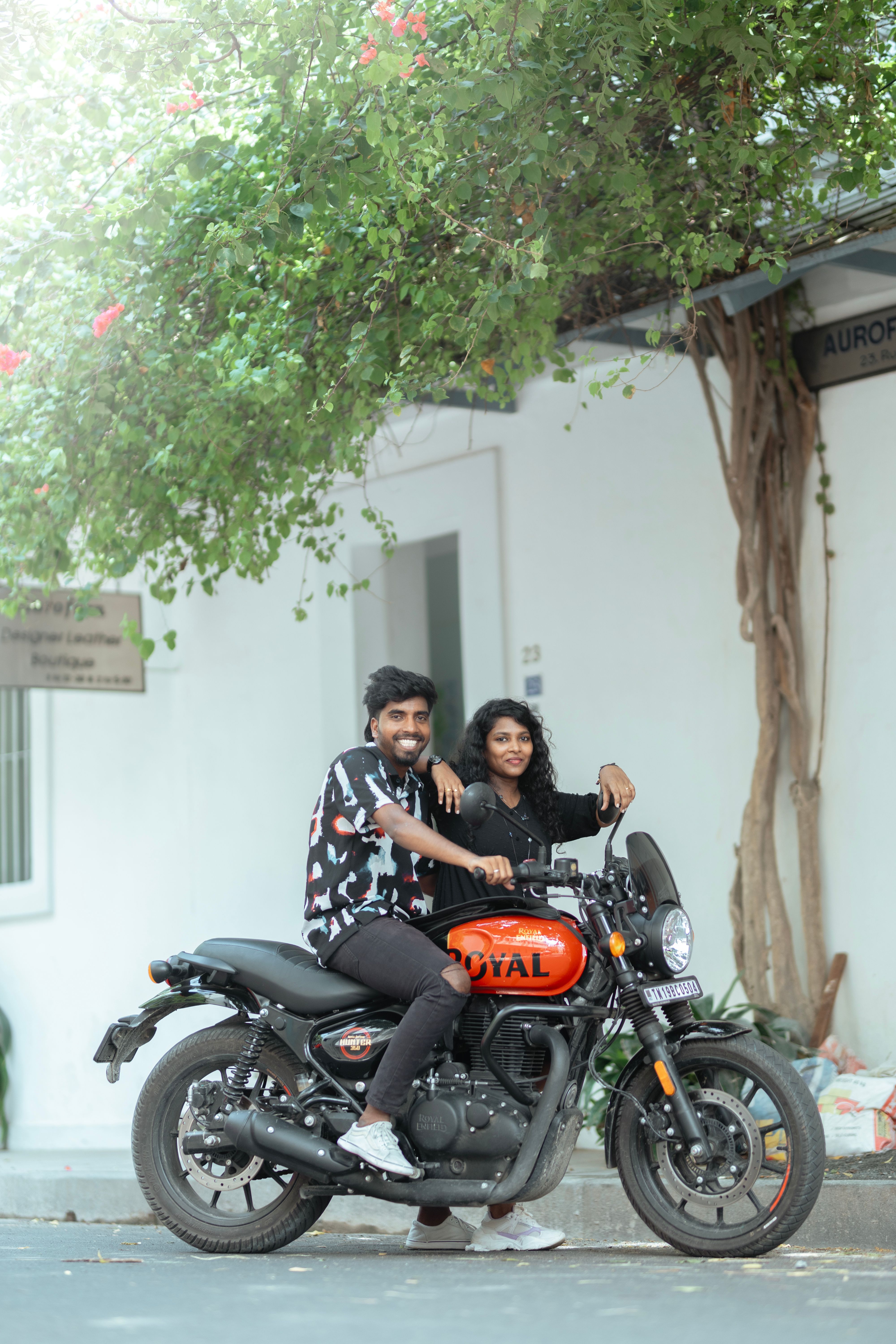 Young couple smiling and seated on a motorcycle outdoors surrounded by greenery.