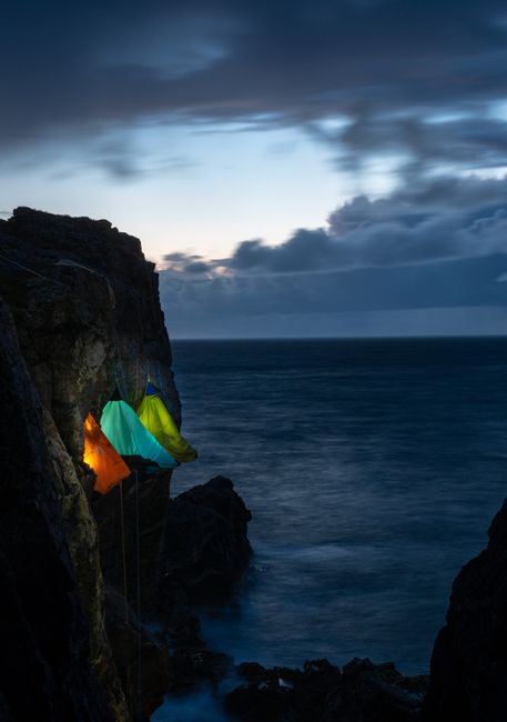Tents on a cliff edge with ocean view at twilight, capturing adventure and serenity.