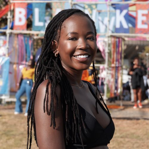 Free A joyful woman with long braids smiling at an outdoor festival under a colorful banner. Stock Photo