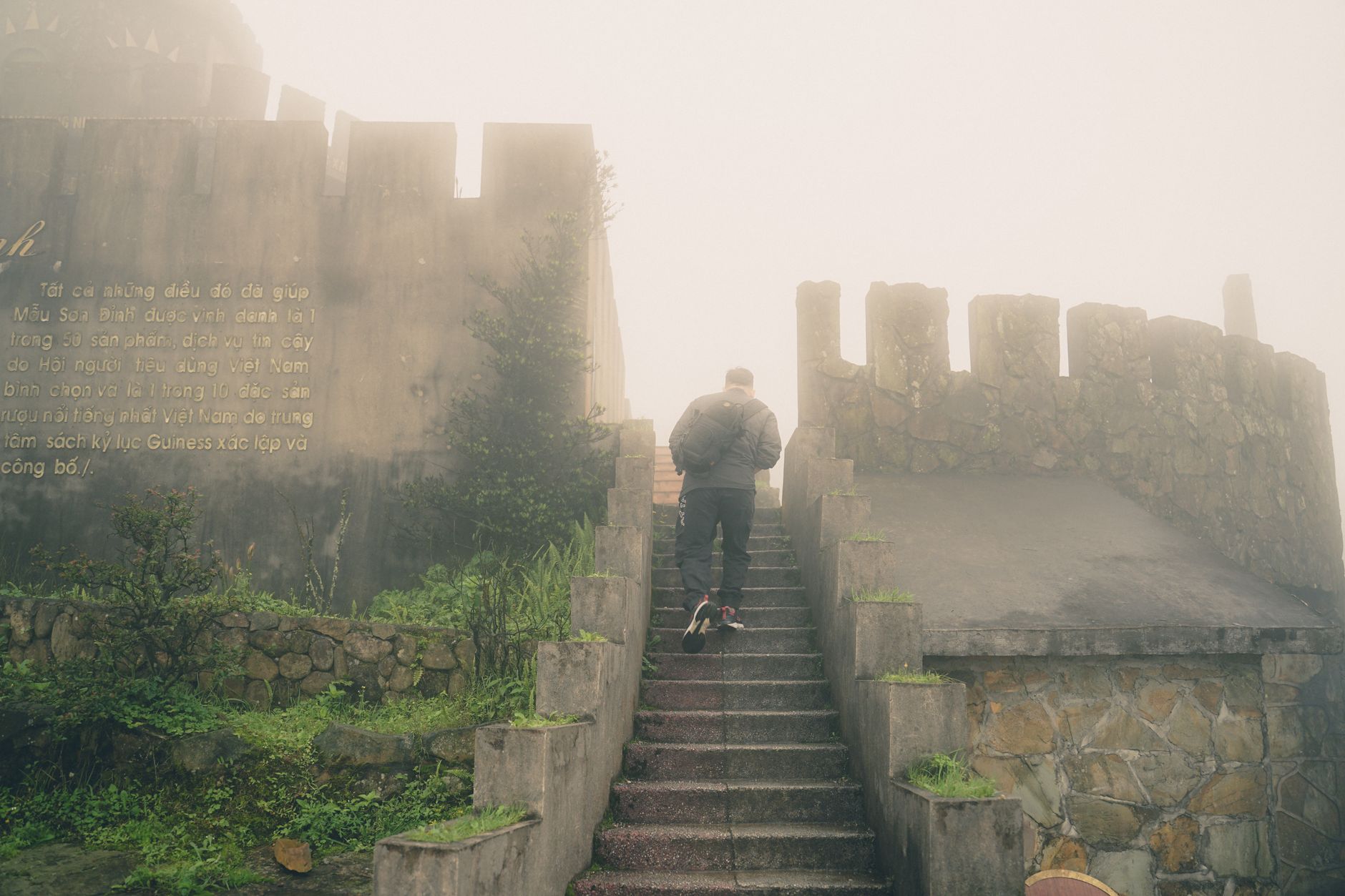 A man ascends a misty stone staircase surrounded by fog and ancient walls, capturing a mysterious atmosphere.