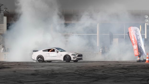 White Ford Mustang drifts, creating smoke at an auto event in Erbil, Iraq.