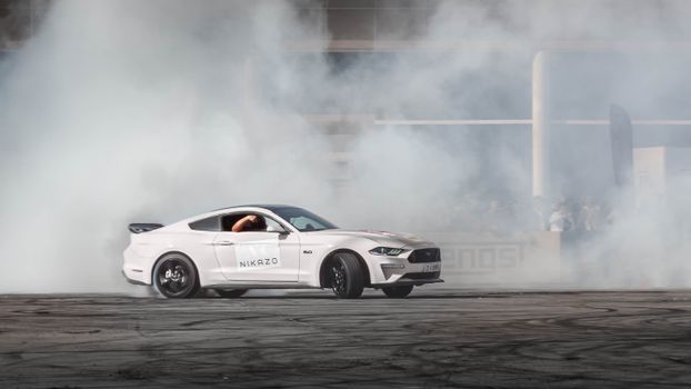 A powerful white car performing a drift maneuver creating dramatic smoke effects outdoors.