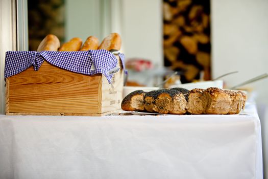 Artisan breads on a wooden tray and tablecloth, showcasing fresh bakery goods indoors.