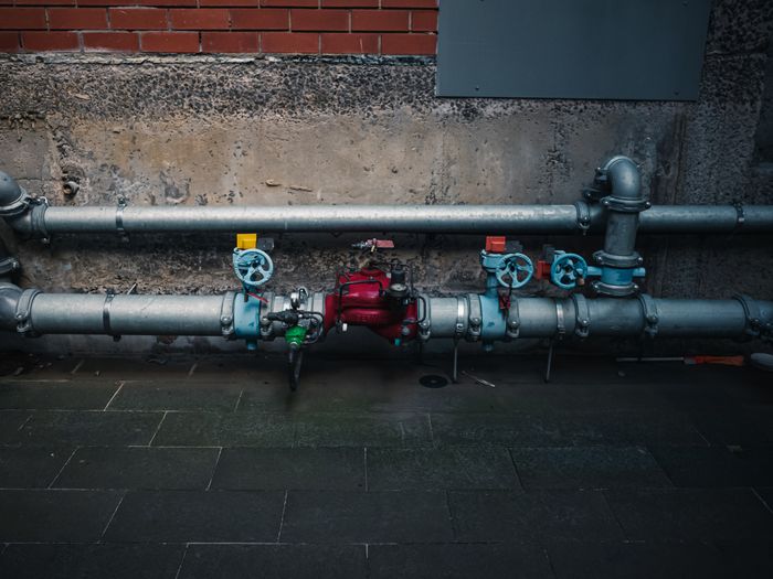 Commercial plant room pipework with isolation valves and gauges along a wall