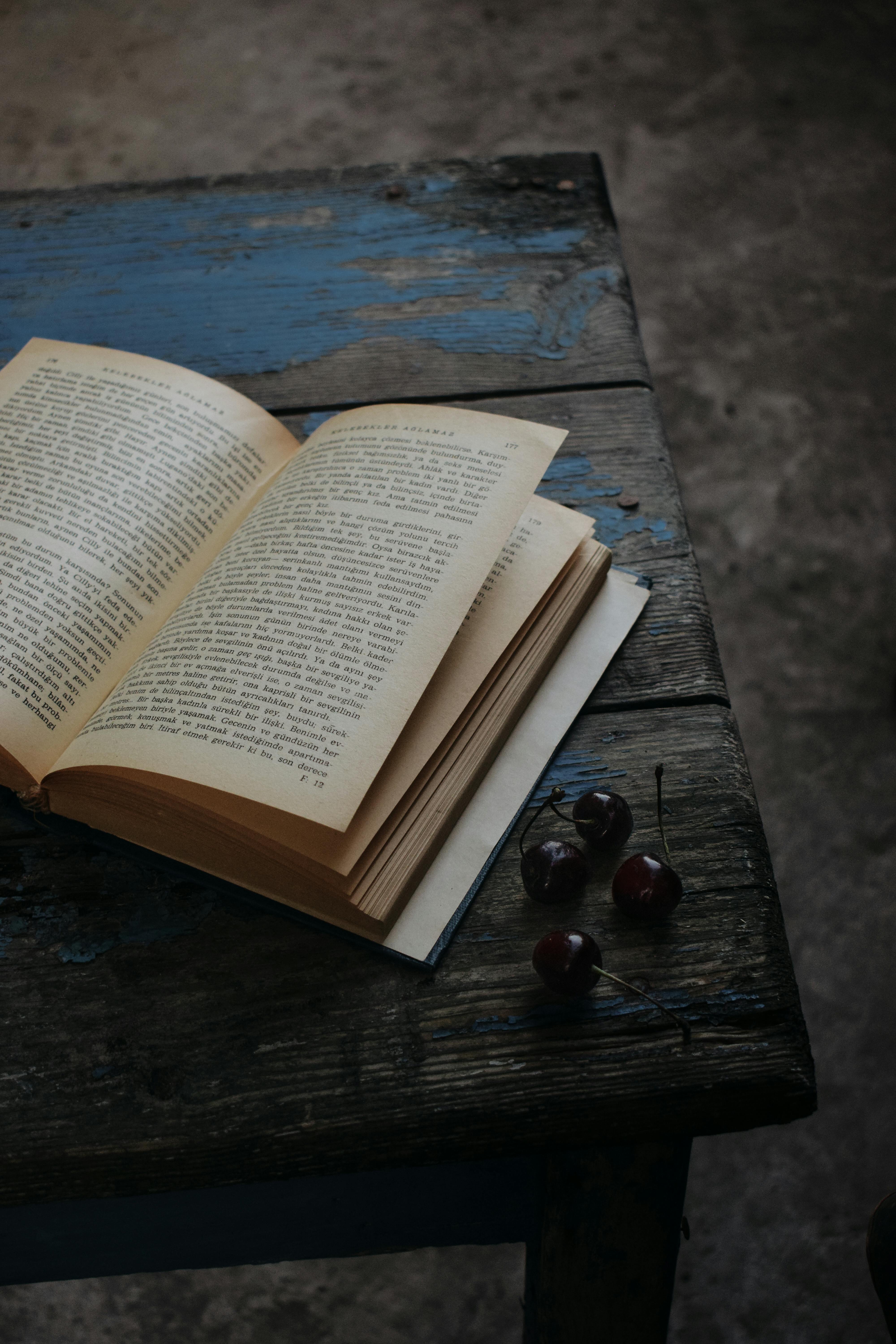 A vintage book open on a rustic wooden table with cherries, creating a classic and nostalgic atmosphere.