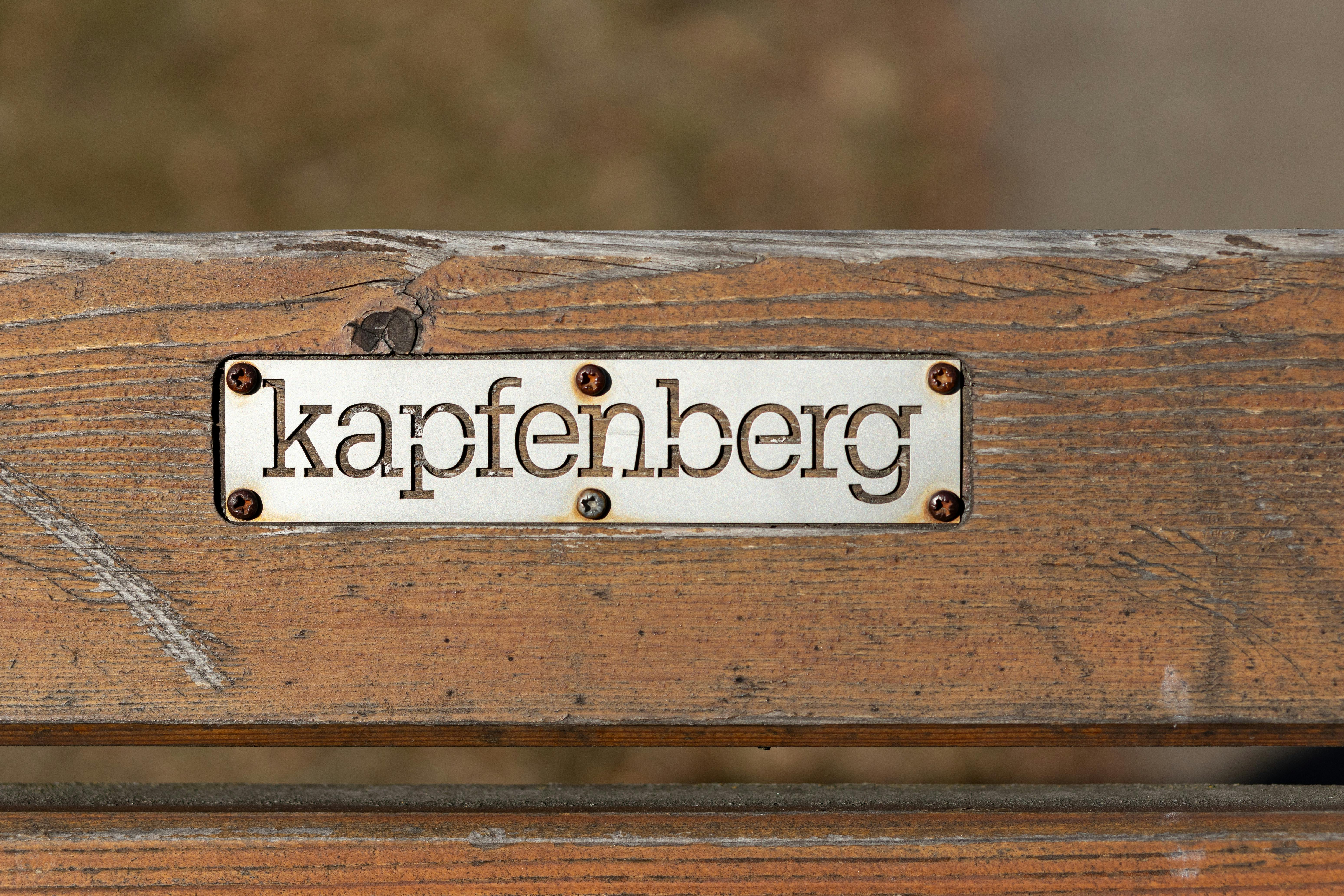 Close-up of a wooden bench with a Kapfenberg plaque detail, outdoors.