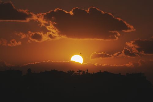 Free Beautiful sunset with silhouetted cityscape and vibrant clouds creating a dramatic skyline. Stock Photo