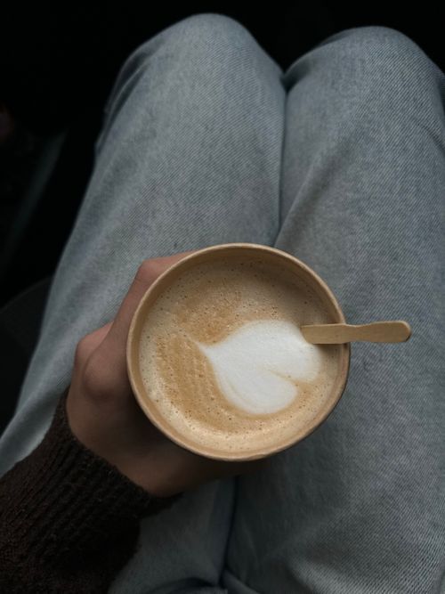 Free Top-view of a warm cappuccino with latte art, held over cozy gray fabric pants. Stock Photo