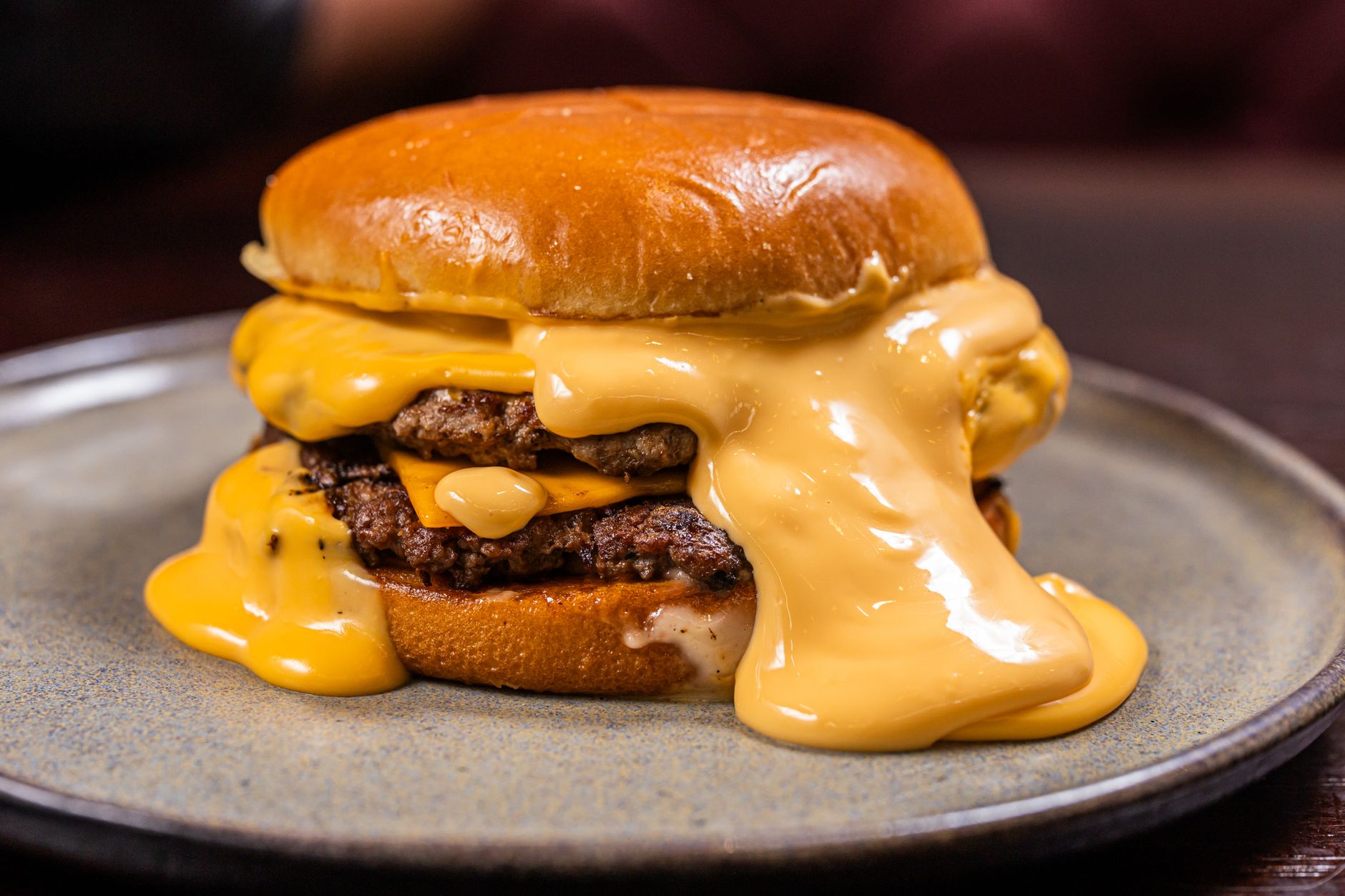 Double-stacked smash burger with melted American cheese, thin onion slices, and lettuce on a toasted brioche bun, showing the characteristic crispy lacey edges of the beef patties