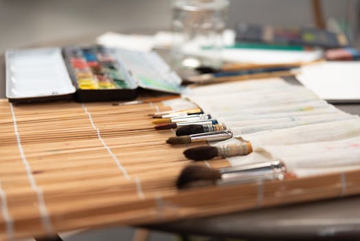 A collection of paint brushes and watercolor set on a bamboo mat, ready for artistic creation.