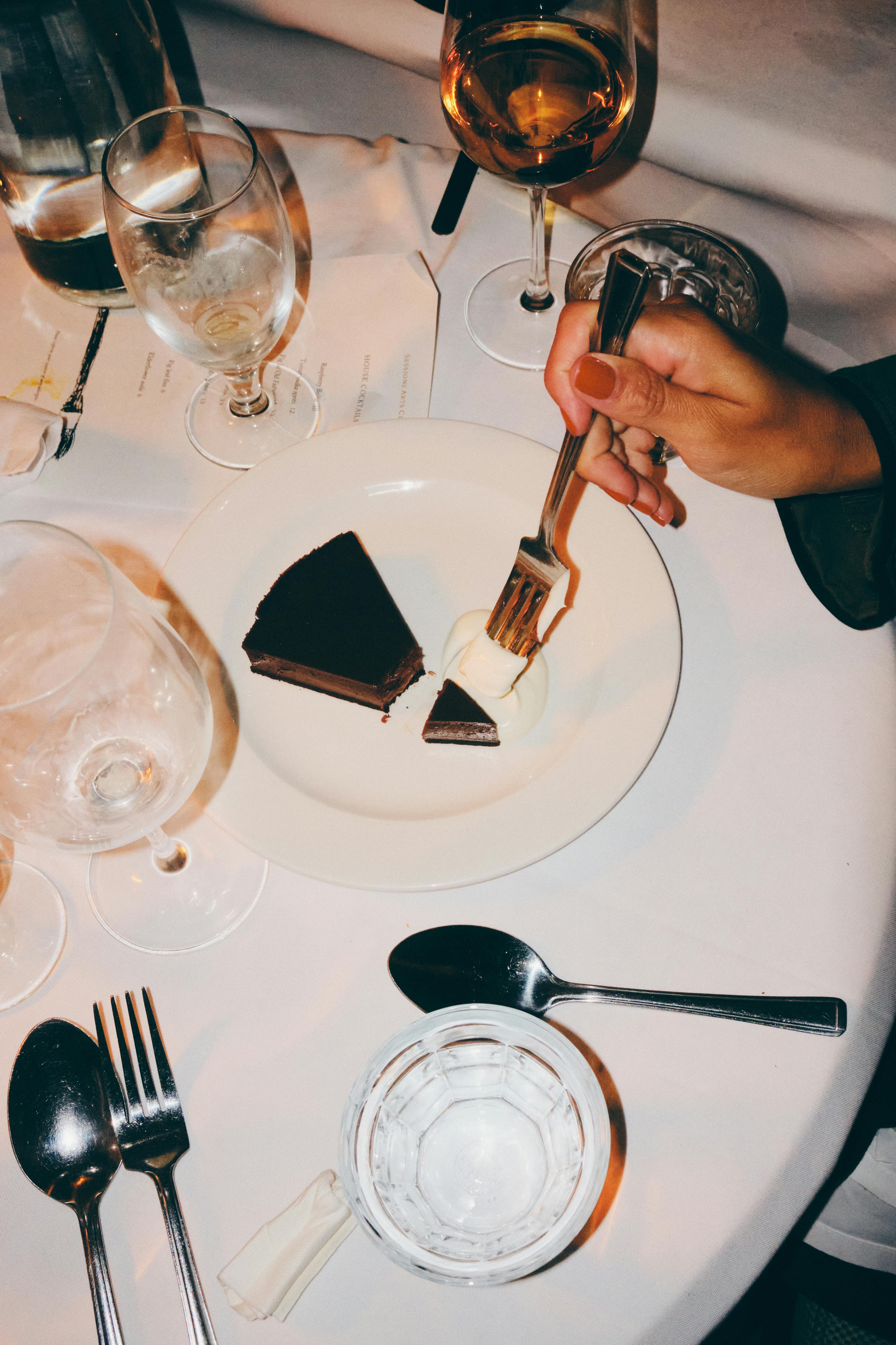 A hand enjoying chocolate cake at an elegant dinner setting.