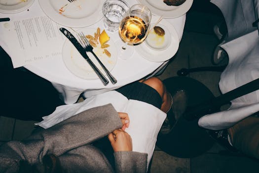 A top-down view of a dining table with elegant table setting and a glass of white wine.