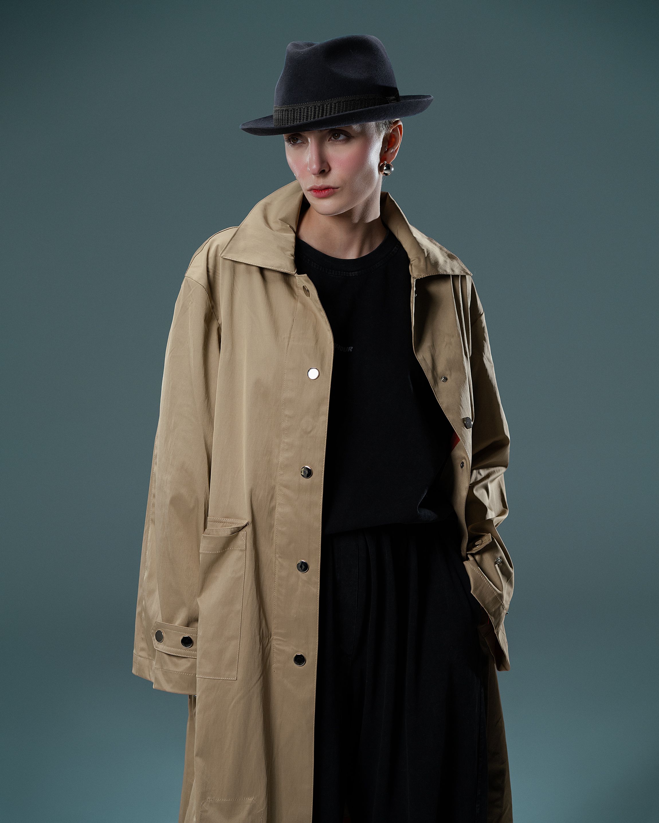 Elegant portrait of a woman in a tan trench coat against a simple backdrop.
