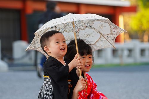 Free Two children in vibrant traditional clothing sharing a lace umbrella outdoors. Stock Photo